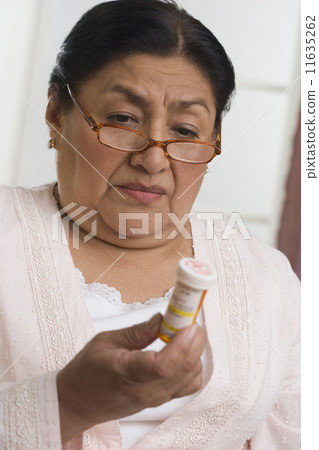 Senior Hispanic woman looking at medication bottle Senior Hispanic woman looking at medication bottle 11635262