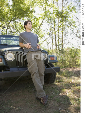 Young man leaning on jeep in woods Young man leaning on jeep in woods 11635373