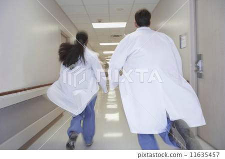 Rear view of doctors running down corridor in hospital 11635457