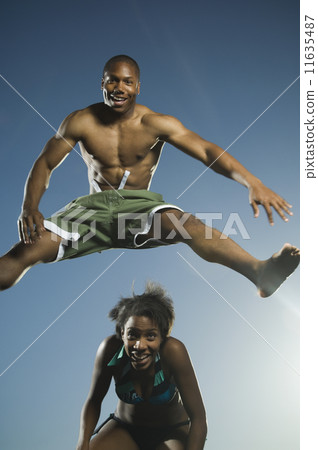 African American man in bathing suit jumping over woman 11635487