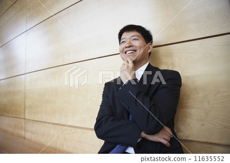 Asian businessman leaning on the wall smiling 11635552