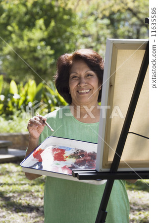 Senior Hispanic woman painting with easel outdoors 11635586
