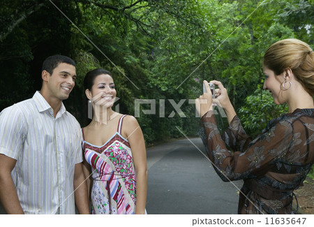 Hispanic woman taking photograph of couple 11635647