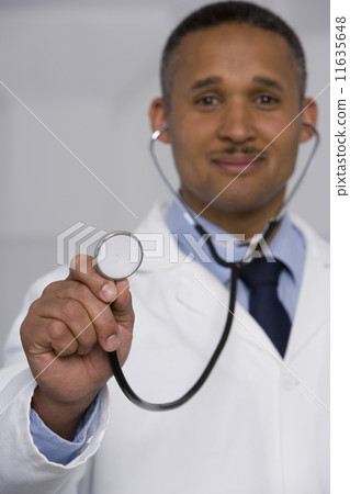 African male doctor holding up stethoscope 11635648