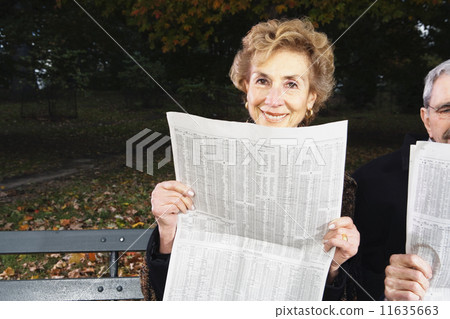 Senior couple reading newspapers on bench outdoors 11635663