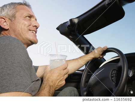 Mature man drinking while driving convertible 11635692