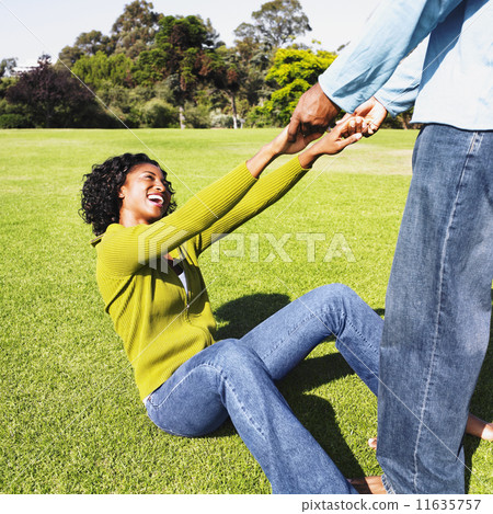 African man helping girlfriend up off grass 11635757