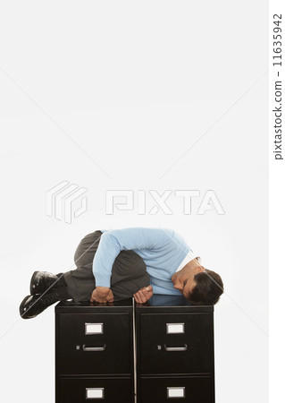 Businessman sleeping on top of filing cabinet 11635942