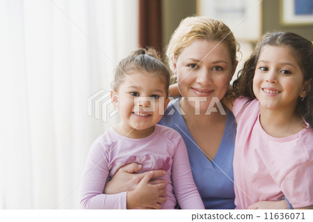Hispanic mother hugging daughters indoors Hispanic mother hugging daughters indoors 11636071