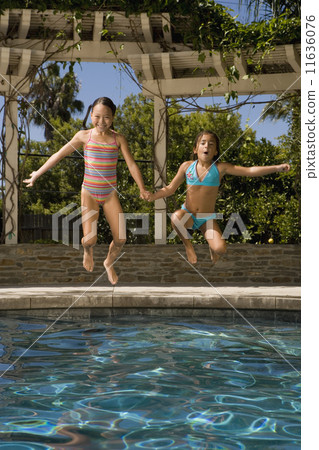 Two girls jumping into swimming pool 11636076