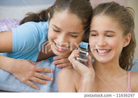 Hispanic sisters using same cell phone 11636297