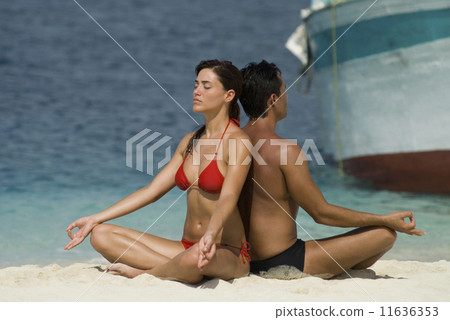 Multi-ethnic couple meditating at beach 11636353