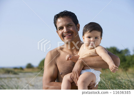 Hispanic father holding baby at beach 11636385