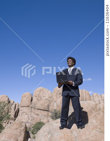 African businessman standing on rock holding laptop 11636404