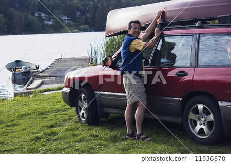 Portrait of man securing boat on top of car at lake 11636870