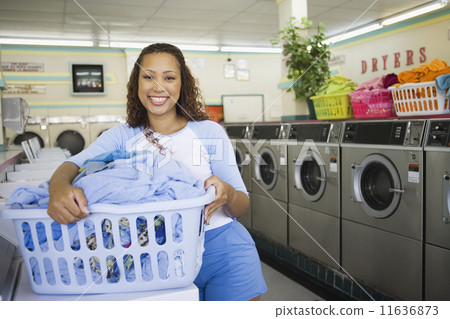Portrait of woman with basket of clothes in laundromat 11636873