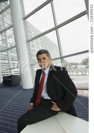 Hispanic businessman sitting on edge of table Hispanic businessman sitting on edge of table 11636915