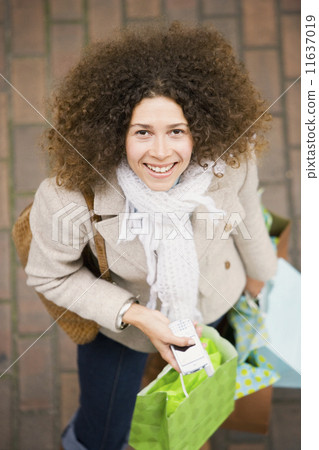 Hispanic woman holding cell phone and shopping bags 11637019