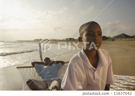 African father and son in hammock at beach 11637042