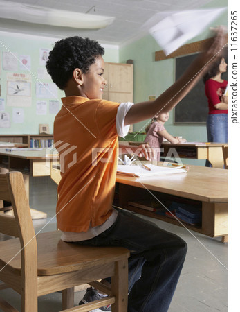 Mixed Race boy throwing paper airplane in class 11637265