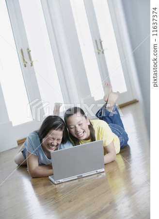 Two teenage girls lying on the floor working on a laptop 11637374