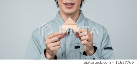一個穿著工作服的男人擁有一棟用木塊搭建的房子。 11637769