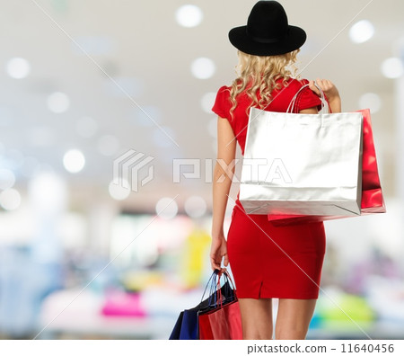 Blond woman in hat and red dress with shopping bags in shop interior 11640456