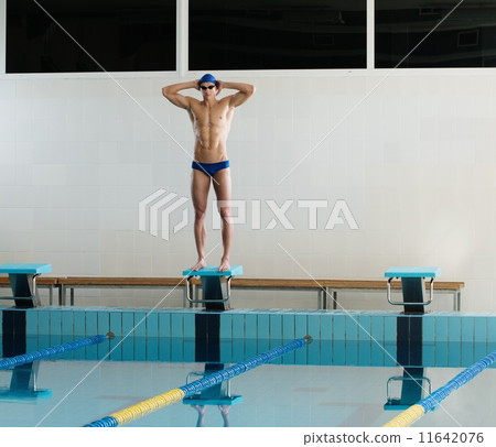 Young muscular swimmer standing on starting block in a swimming pool Young muscular swimmer standing on starting block in a swimming pool 11642076