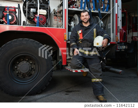 Cheerful firefighter near truck with equipment Cheerful firefighter near truck with equipment 11642112