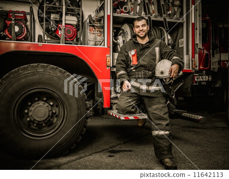 Cheerful firefighter near truck with equipment Cheerful firefighter near truck with equipment 11642113