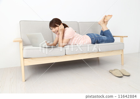 A woman lying down on the sofa and watching a computer 11642884