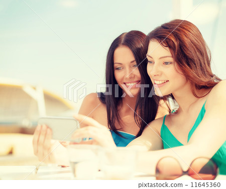 girls looking at smartphone in cafe on the beach girls looking at smartphone in cafe on the beach 11645360