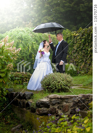Married couple standing under umbrella at park Married couple standing under umbrella at park 11670716