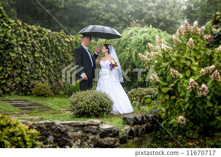 Bride and groom walking under umbrella at park Bride and groom walking under umbrella at park 11670717