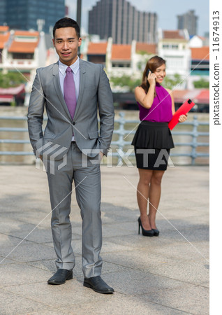 A young and dynamic Chinese male executive stand forward while his female co-worker is on the phone A young and dynamic Chinese male executive stand forward while his female co-worker is on the phone 11674913