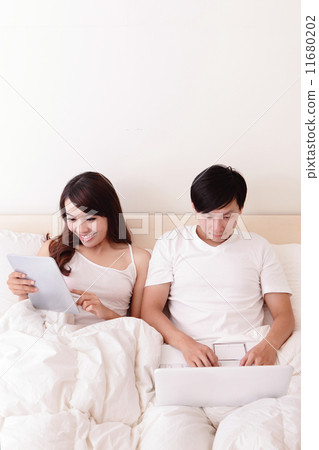 Cheerful couple using touch pad in bed 11680202