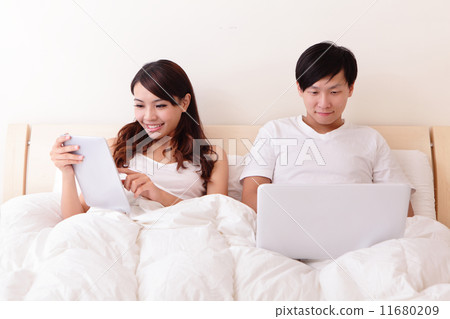 Cheerful couple using touch pad in bed 11680209