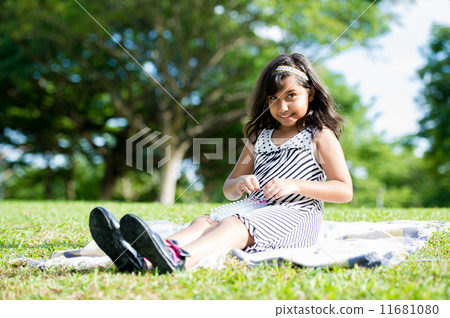 Young asian girl happily playing on the picnic mat in the park Young asian girl happily playing on the picnic mat in the park 11681080