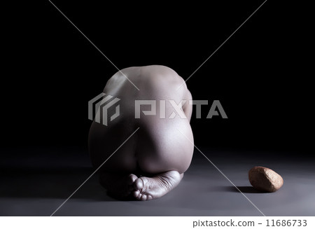 Rear view of slim naked woman posing next to stone 11686733