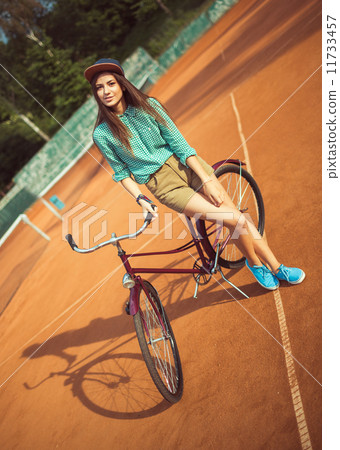 Girl hipster standing with magenta bike on the tennis court 11733457