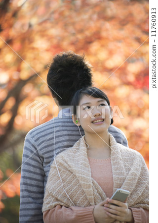 A couple listening to music in front of autumn leaves 11760913