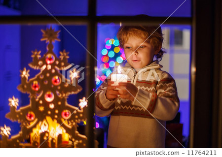Little boy standing by window at Christmas time and holding cand Little boy standing by window at Christmas time and holding cand 11764211