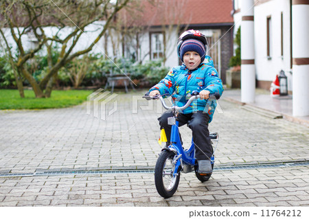 Happy boy of three years riding on bicycle in autumn or winter, 11764212