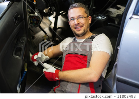 Cheerful mechanic with wrench fixing something in a car interior Cheerful mechanic with wrench fixing something in a car interior 11802498