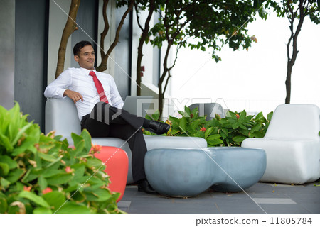 Successful young Indian corporate executive using laptop sitting down along a promenade 11805784