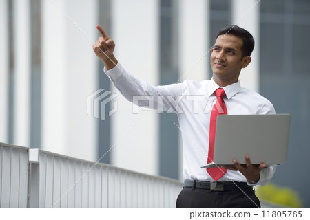 Successful young Indian corporate executive using laptop in front of concrete building 11805785