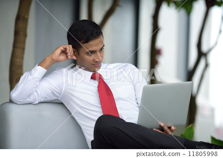 Successful young Indian corporate executive shocked while using laptop sitting down along promenade Successful young Indian corporate executive shocked while using laptop sitting down along promenade 11805998