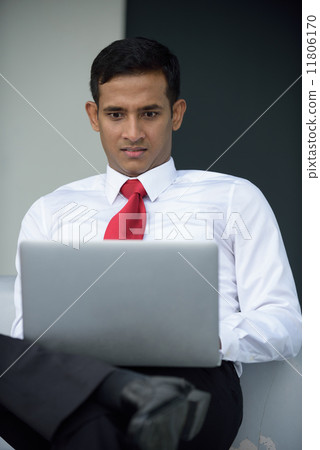 Successful young Indian corporate executive shocked using laptop sitting down along promenade 11806170