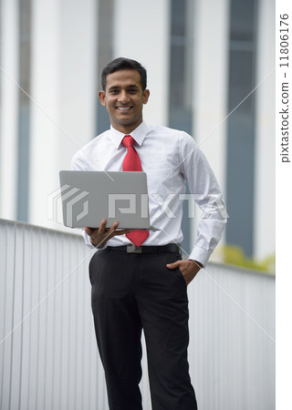 Successful young Indian corporate executive using laptop in front of concrete building Successful young Indian corporate executive using laptop in front of concrete building 11806176