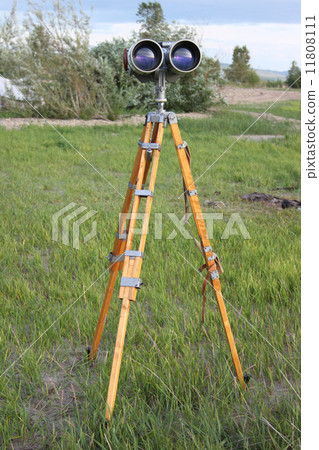 A binoculars with a tripod with a azimuth head in a forest on a sand with grass A binoculars with a tripod with a azimuth head in a forest on a sand with grass 11808111